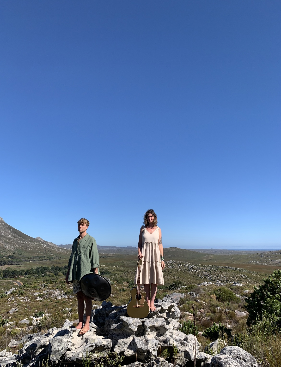Genevieve and Milo standing on rocks in the fynbos with guitar and handpan
